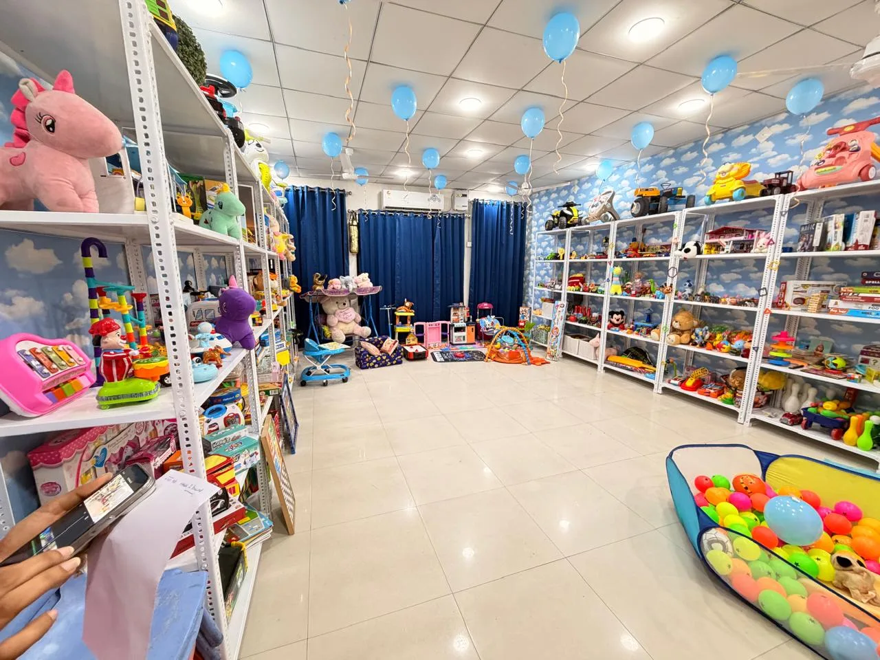 Inside Chahak Toy Library: white shelves full of toys against a sky-blue cloud wallpaper, with a ball pit and play corner